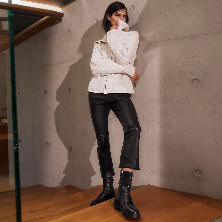 Woman wearing Autograph cream cable-knit jumper, black leather trousers and boots. Shop Autograph