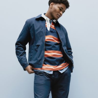 Man wearing an orange and navy striped rugby shirt, blue chinos and jacket. Shop the collection