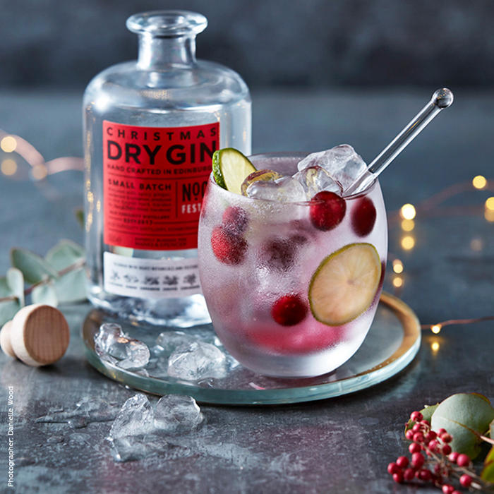 Bottle of Christmas dry gin with a G&T garnished with lime and clementine