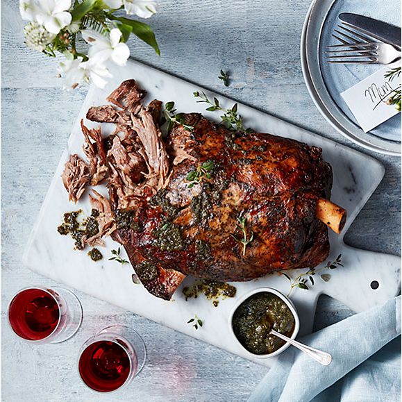 Slow-cooked lamb shoulder with mint sauce, two glasses of red wine and spring flowers