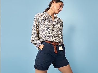 Woman wearing a printed blouse and navy shorts with a tan waist belt