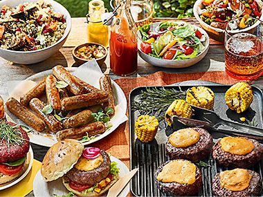 A barbecue spread including burgers, sausages and a selection of salads